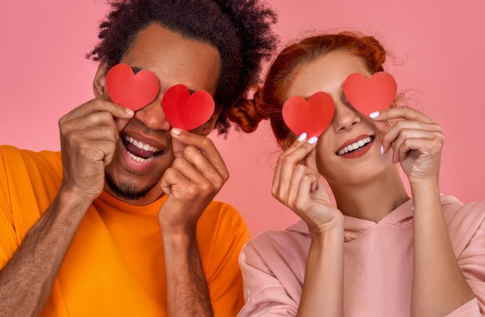 interracial couple holding paper hearts before their eyes